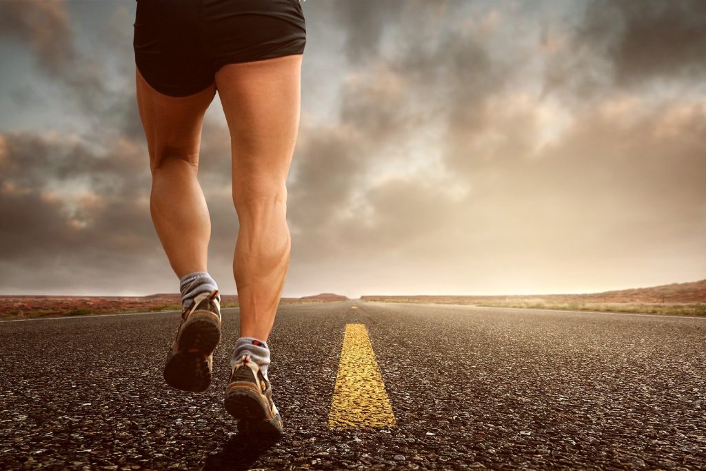 Un homme de dos dont on voit juste les jambes courant sur une route à perte de vue