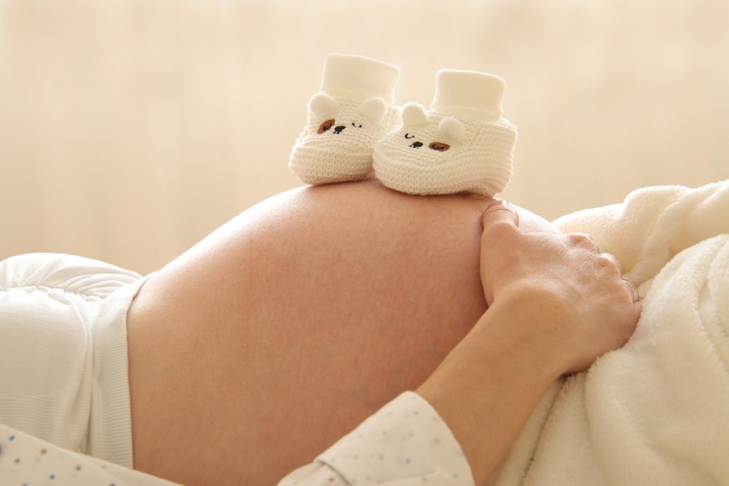 Ventre de femme enceinte allongée, avec une paire de chaussons d'enfant en laine posés dessus